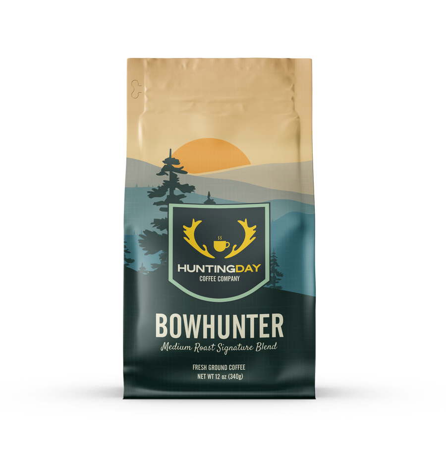 A bag of Huntingday Coffee Company 'Bowhunter' medium roast coffee, featuring a landscape design with a golden sun, pine trees, and a dark teal mountain range.