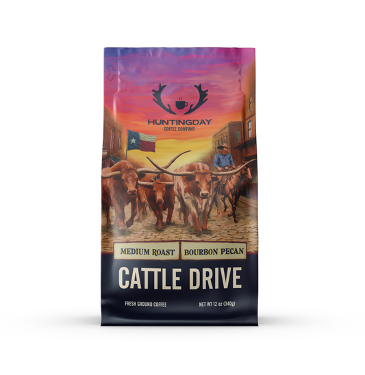 A 12 oz bag of Huntingday Coffee Company Cattle Drive medium roast coffee, featuring a colorful graphic illustration of longhorn cattle on a cobblestone street with a cowboy riding behind them under a sunset sky.
