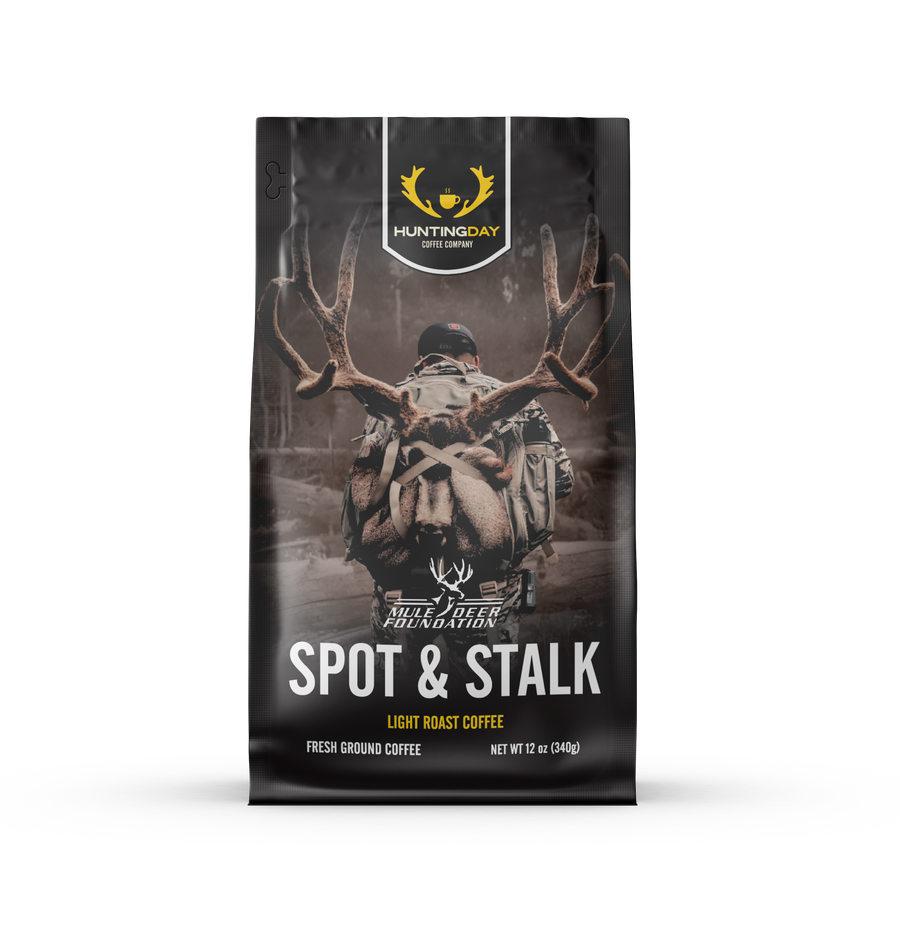 A 12 oz bag of Huntingday Spot & Stalk light roast coffee, featuring a dark, moody graphic of a deer with large antlers on a forest background.